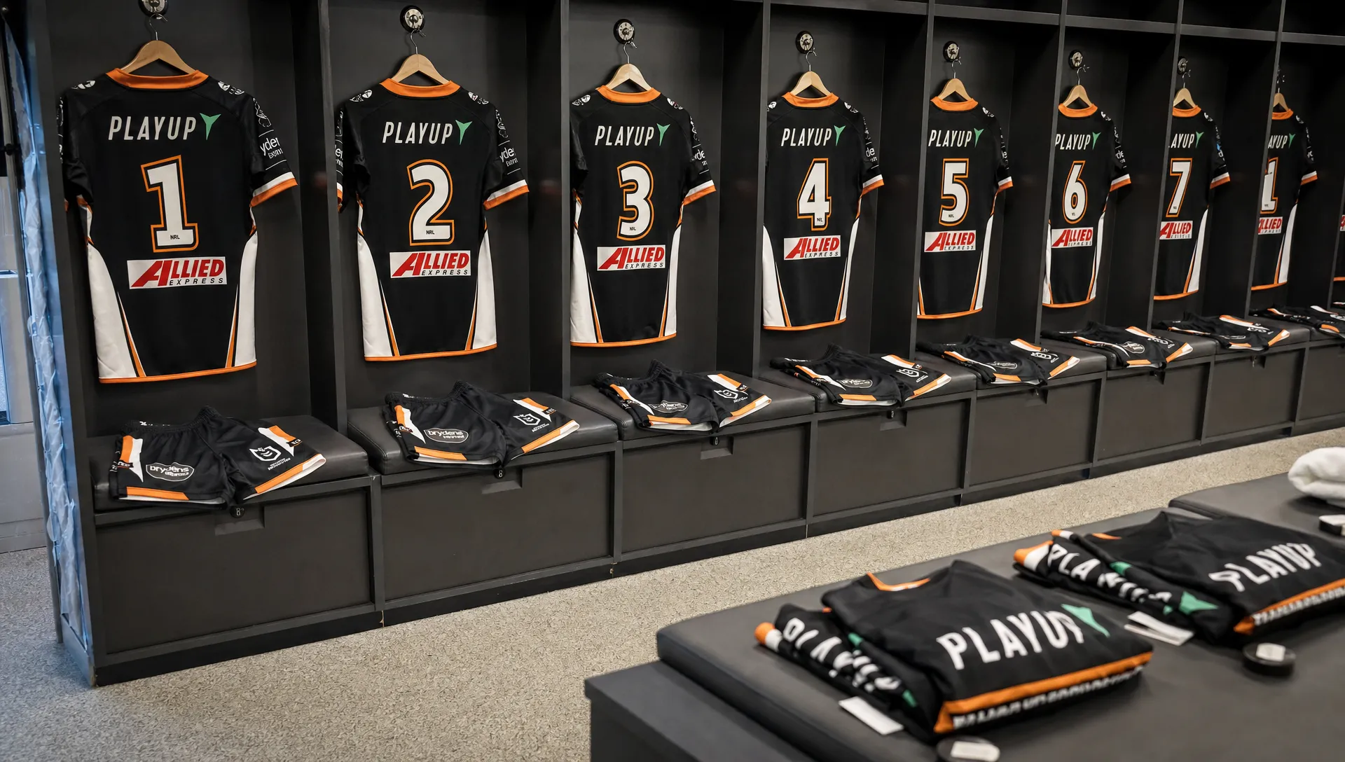 Rugby league uniforms are laid out in a locker room with jerseys, shorts and socks, showing numbers, sponsor areas and reinforced matchwear details.