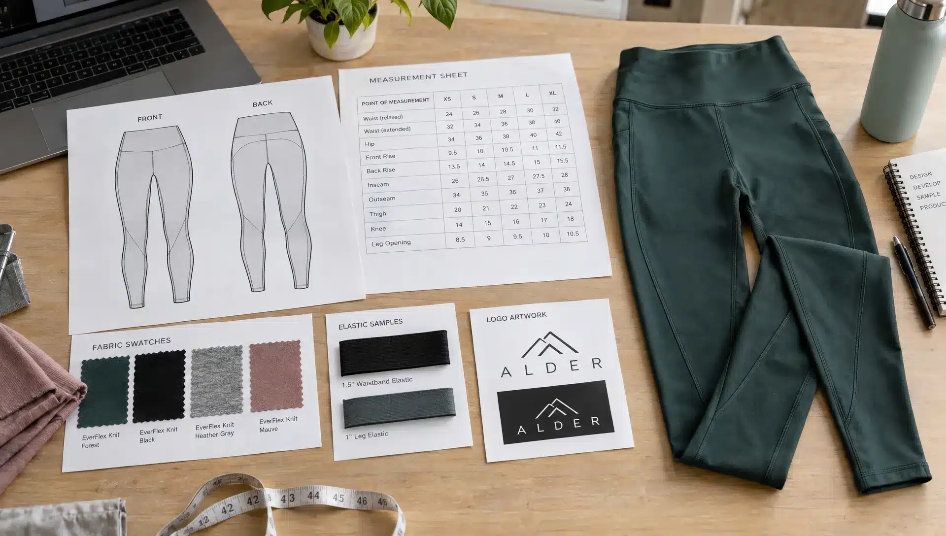 Front and back legging technical drawings, a measurement sheet, fabric swatches, elastic samples and logo artwork sit beside a finished sample garment on a designer’s worktable.